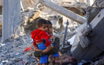 Seorang anak laki-laki Palestina sambil menggendong balita berdiri di lokasi serangan Israel saat konflik yang sedang berlangsung antara Israel dan kelompok perlawanan Palestina Hamas di Rafah, di selatan Jalur Gaza, Senin (4/12/2023). (ANTARA FOTO/REUTERS/Mohammed Salem/Spt.)